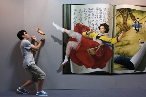 A man poses for a photograph near a 3D painting at the 2012 Magic Art Special Exhibition in Hangzhou